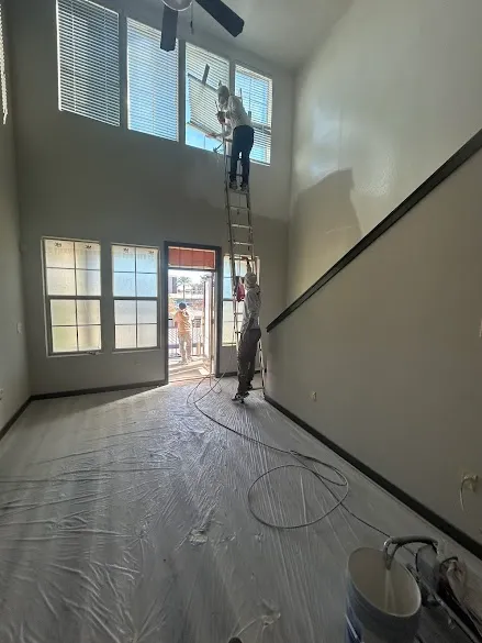 JAE Painting & Restorations crew spray painting a two-story living room in Phoenix with floors fully masked